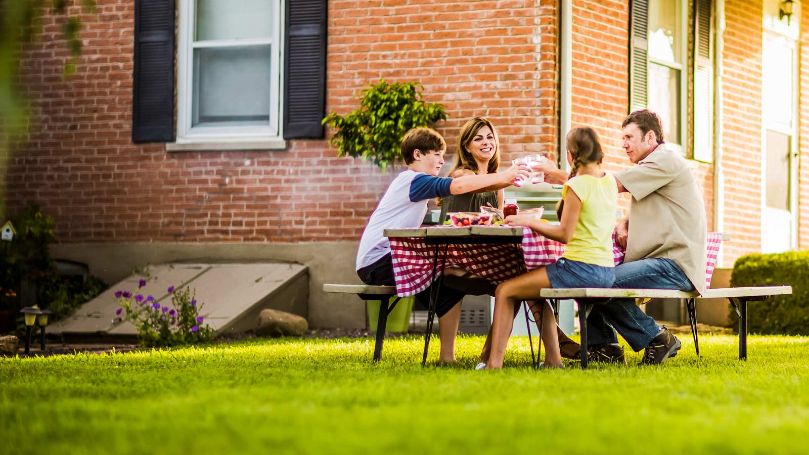 A family enjoys a meal on a picnic bench outside on their bright and green lawn